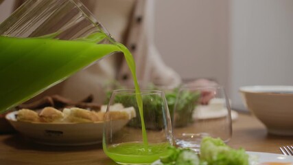 Closeup of fresh green juice being poured into glass on breakfast table with healthy food and fresh vegetables, capturing wholesome morning and healthy lifestyle