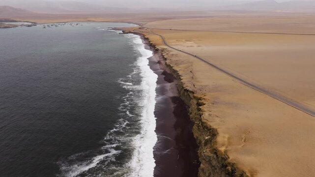 Pale sand narrows into a sweeping point where surf breaks rhythmically along the Paracas coast, aerial pullback as waves crash
