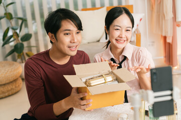 Unboxing livestream asian couple home studio smartphone vlog influencer happy product review box content creator. Energetic duo share unboxing moment cozy room engaging audience with genuine