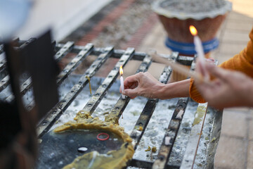 Serene close up of hand lighting candle with bright flame. spiritual worship ceremony showing an act of faith and reverence at an outdoor temple, moment of peace