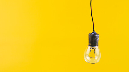 An unlit incandescent light bulb rests on a simple isolated on yellow background
