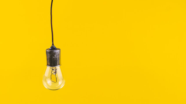 An unlit incandescent light bulb rests on a simple isolated on yellow background