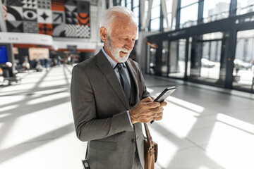 Senior Businessman Using Smartphone in Modern Airport Terminal