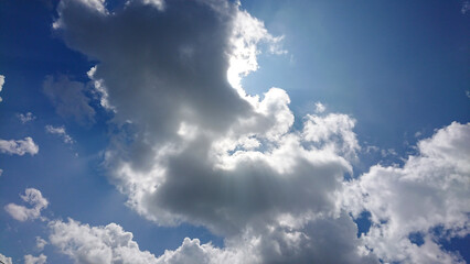 Bright sun rays pierce cumulus clouds in a vivid blue sky, creating dramatic light and shadow contrasts.