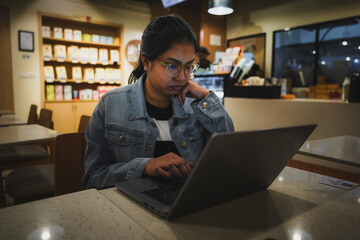 Indian woman working on a laptop in a coffee shop, focused on her tasks in a modern work-friendly environment.