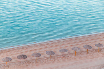 Sunny beach with straw umbrellas lined along the shore near clear blue water