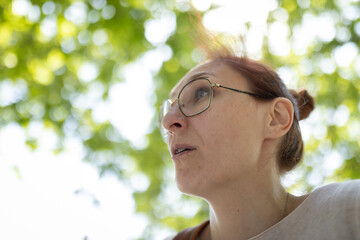 Woman with glasses looking up observing green leaves