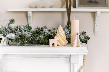 Minimalist Christmas decor with frosted garland, candles, and festive ornaments on a white mantel.