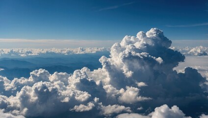 Aerial view of dramatic cumulus clouds over mountains. Blue sky with towering cloud formations above landscape. Scenic cloudscape horizon above distant mountain range.