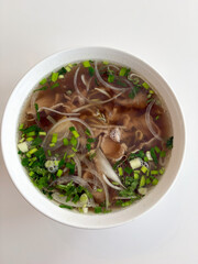 Vietnamese pho noodle soup with beef and herbs in white bowl  