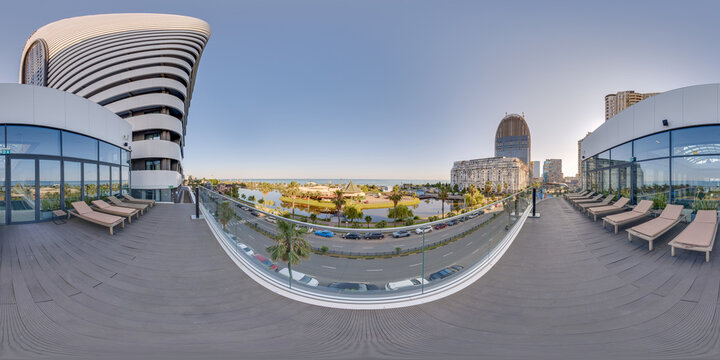 Equirectangular 360 photo of a large hotel or residential rooftop terrace with numerous empty sun loungers. Offers a clear view of the Batumi cityscape, Sherif Khimshiashvili Street, and the seaside. 