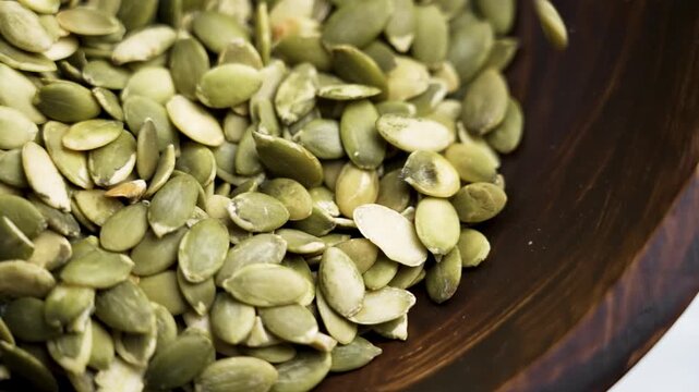 Green pumpkin seeds falling onto the rustic wooden texture of a bowl in slow motion