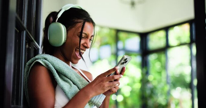Fist pump, fitness and phone with woman in home for surprise reaction to text message news. App, celebration and wow with excited person in headphones for music streaming or notification alert