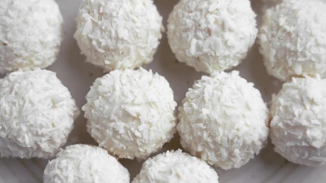 Coconut truffles covered with white coco chips on ceramic plate. Sweet yummy balls. Rotation