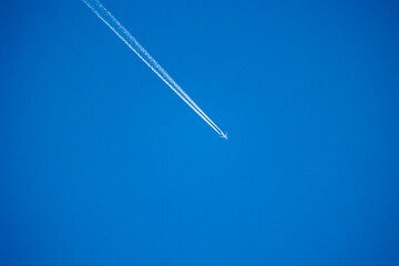 A beautiful white plane crossing clear blue skies over Latvia, Europe. Sunny day with plane trails.