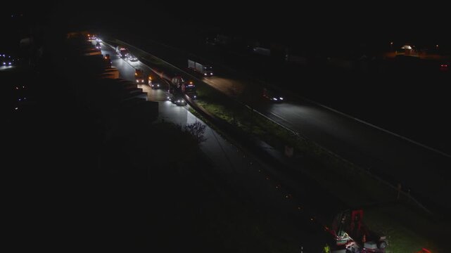 Spectacular heavy transport of a wind turbine rotor blade at night on a multi-lane highway. The oversized truck is illuminated by escort vehicles on the dark road.