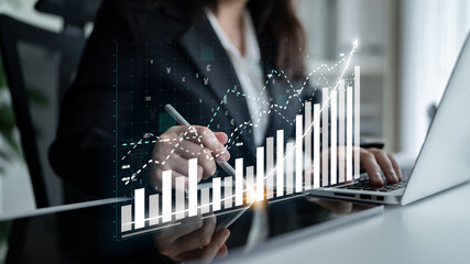 A business professional uses a laptop to analyze financial data with a growing graph overlay, highlighting trends and success in a modern office setting. Impute