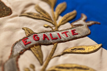 D&eacute;tail d'un vieux drapeau fran&ccedil;ais sur lequel est &eacute;crit le mot " &eacute;galit&eacute; " en rouge.