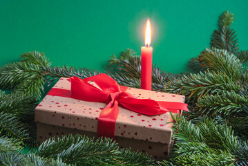 Christmas gift box with burning candle in between fir branches on green background