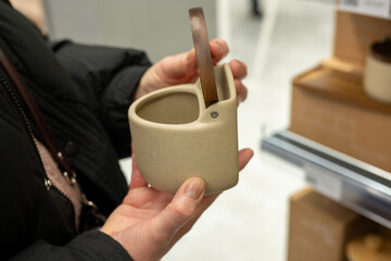 Woman handling beige ceramic mug with wooden handle in store
