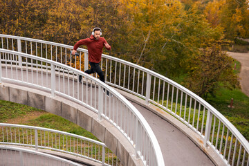 Man Running on Curved Path in Autumn Park Using Headphones