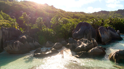 Tropical beach with smooth granite rocks, palm trees, and clear turquoise water at sunset shoreline