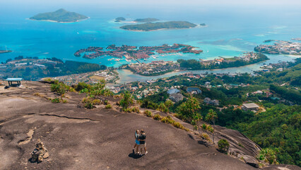 Couple embraces on a mountaintop overlooking a tropical island village and turquoise sea panorama from a high vantage point