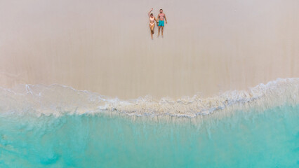 Aerial view of couple lying on sunny beach beside turquoise ocean and gentle waves together