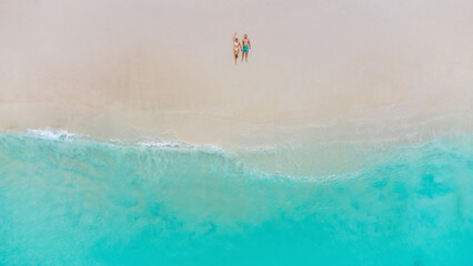 Aerial view of couple relaxing on sandy beach with turquoise ocean and calm waves today