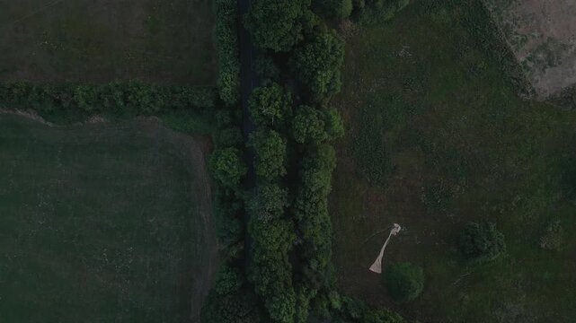 An aerial view of a road bordered by trees and fields. A large, light-colored object lies on the grass, resembling a parachute or a fabric sculpture.