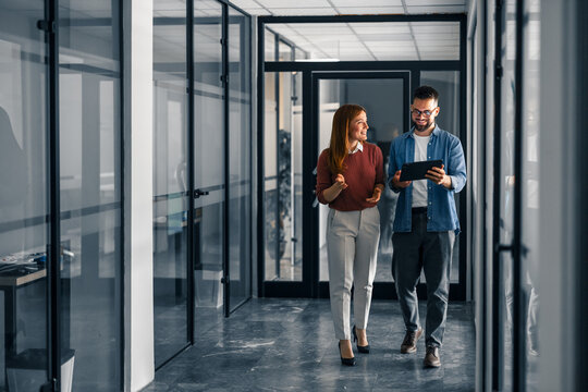 Colleagues Walking Through Office Hallway Discussing Projects on a Digital Tablet