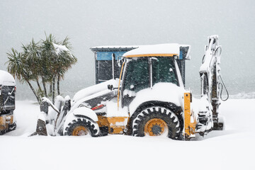 Yellow backhoe loader, commonly used as a type of snow removal equipment, partially covered in snow.