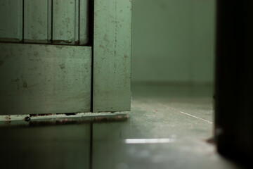 Close-up of the bottom edge of a dusty, old green metal door, reflecting on a polished tile floor. Contrast between rough and glossy surfaces, suitable for industrial/abstract backgrounds