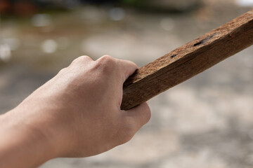 Close-up of a human hand gripping an old, rough piece of wood. Illustrates labor, construction,...