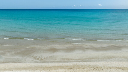 Aerial view of the crystal clear, turquoise sea. The sea stretches to the horizon with colours ranging from azure to dark blue. The coast with its white beach is in the foreground. Sunny summer day.