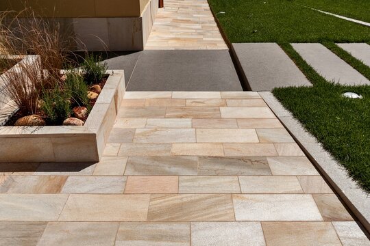 Contemporary outdoor design with beige limestone tiles, concrete inserts, and grass&mdash;clean lines and material contrast.