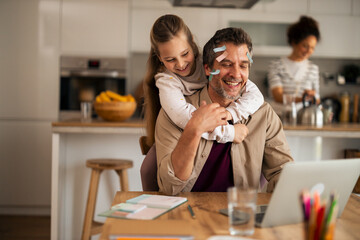 Father Working from Home While Daughter Playfully Interrupts in the Kitchen