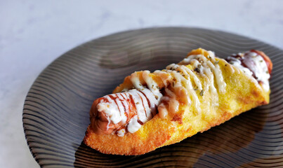 Freshly baked sausage in golden brown pastry roll  topped with mayonnaise and ketchup on a dark...
