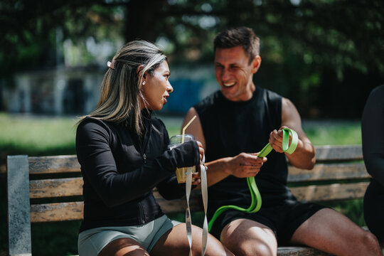 A group of friends seated on a park bench, engaged in fitness activities and conversation, illustrating friendship, teamwork, and a healthy active lifestyle in a relaxed outdoor environment. - Powered by Adobe