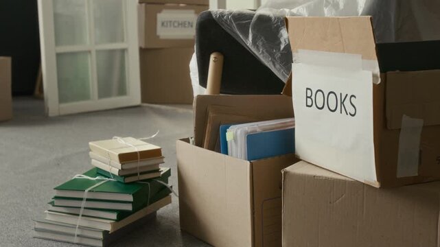 No people tilt down shot of stack of tied books and three moving boxes on carpeted floor of living room