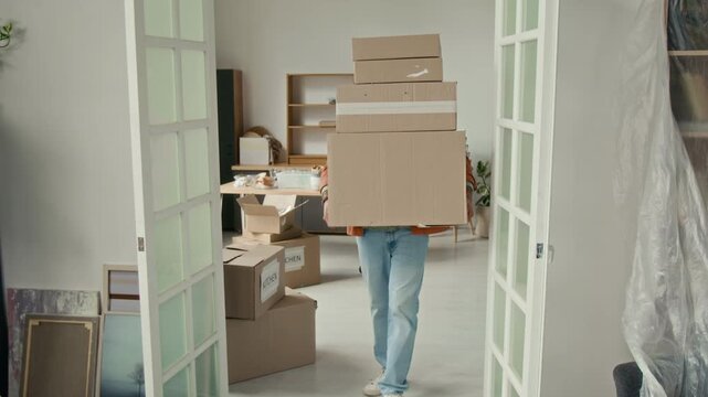Tilt down view of young man carefully carrying four cardboard boxes to room and placing them down during moving process