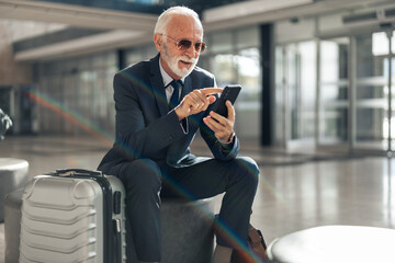 Senior Businessman Using Smartphone at Airport Lounge with Suitcase Nearby