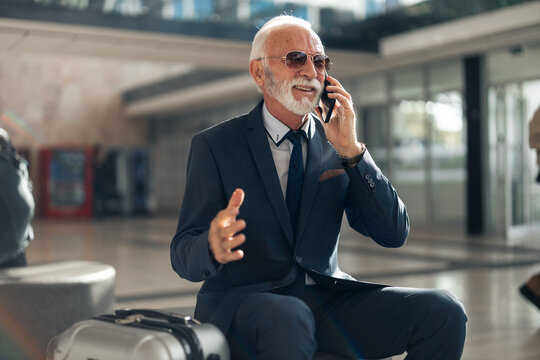 Elderly Businessman Talking On Phone In Lounge Area With Luggage - Powered by Adobe