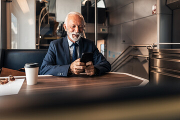 Senior Businessman Using Smartphone While Traveling in Modern Train