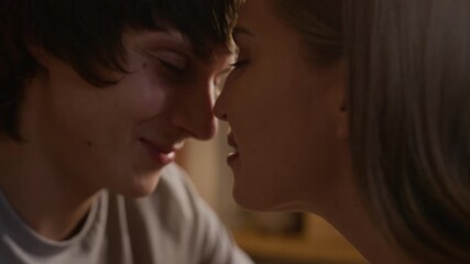 Closeup of affectionate young Caucasian couple sitting close together, kissing tenderly and sharing warm and intimate moment while enjoying each other closeness and romantic connection