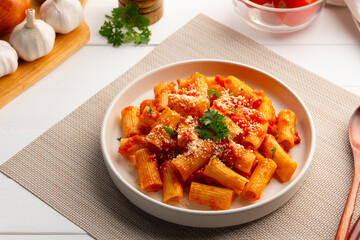 Rigatoni macaroni with fresh tomatoes sauce in white plate.topped with parmesan cheese and parsley.