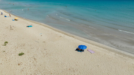 Obraz premium Aerial view of a beautiful sandy beach overlooking a turquoise and crystal clear sea. Beach umbrellas of tourists at San Lorenzo Beach in the Province of Syracuse, Sicily, Italy. Sunny summer morning.