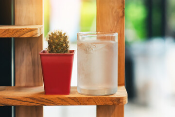 Small glass of cool pure water with little cactus in pot on brown wooden shelves background. Fresh water in the glass and flower pots. Desert and thirsty concept, Drink clear water for health concept.