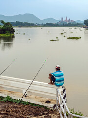 Elderly fisherman at side of river during sunset and catching fish with spinning. Senior fisherman with fishing rods on footbridge near the lake at summer. Mature man fishing on lake. Adult lifestyle.