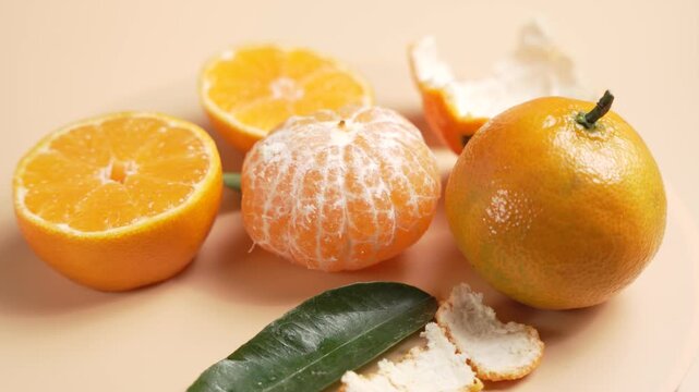 Peeled mandarin rotates beside halved citrus and scattered peel pieces. Bright segments and pith texture create a fresh, tactile food scene.
